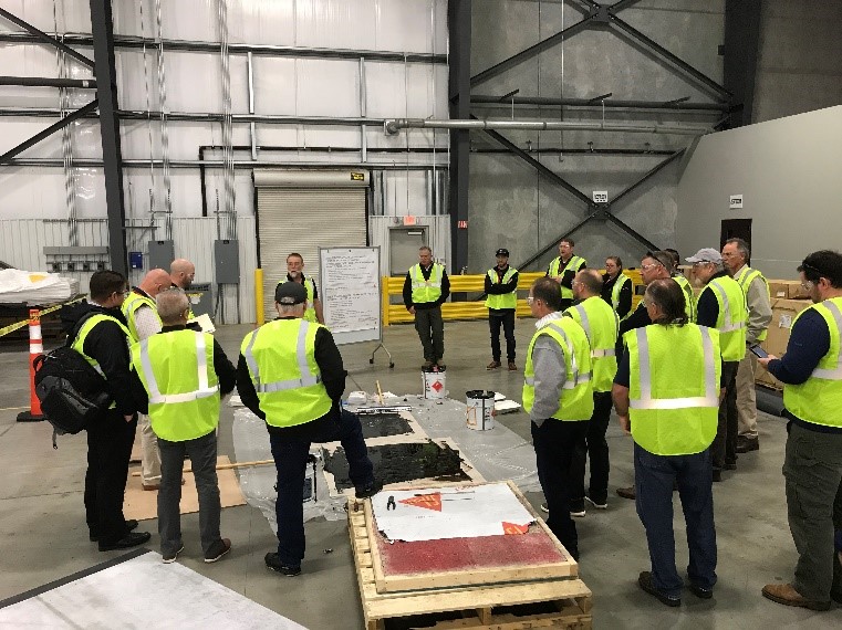 A group of people standing around technical demos in safety vests